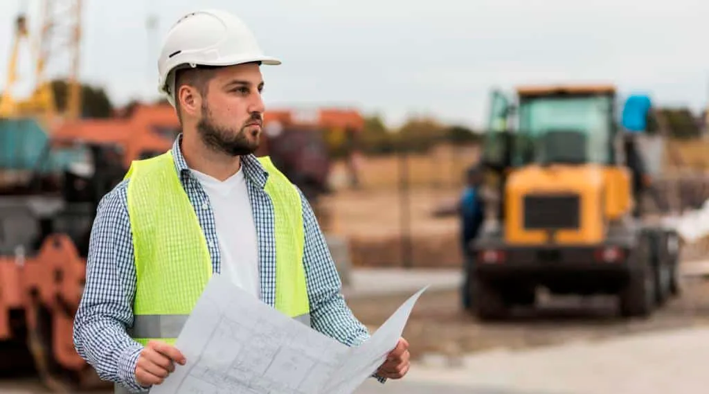 Engenheiro com capacete e planta de obra em canteiro de obras